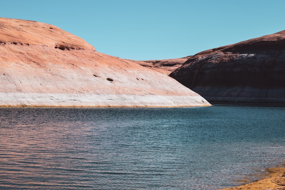 brown rocky mountain beside blue sea under blue sky during daytime