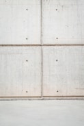 A concrete wall with a grid pattern is formed by the intersection of vertical and horizontal seams. The surface is smooth with visible small, round indentations evenly distributed across the panels. The lower section of the image shows a plain concrete floor.