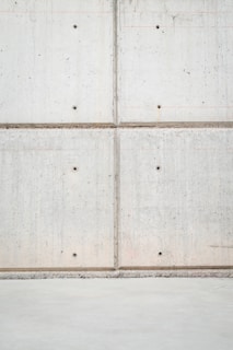 A concrete wall with a grid pattern is formed by the intersection of vertical and horizontal seams. The surface is smooth with visible small, round indentations evenly distributed across the panels. The lower section of the image shows a plain concrete floor.