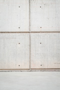 A concrete wall with a grid pattern is formed by the intersection of vertical and horizontal seams. The surface is smooth with visible small, round indentations evenly distributed across the panels. The lower section of the image shows a plain concrete floor.