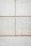 A concrete wall with a grid pattern is formed by the intersection of vertical and horizontal seams. The surface is smooth with visible small, round indentations evenly distributed across the panels. The lower section of the image shows a plain concrete floor.