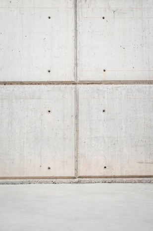 A concrete wall with a grid pattern is formed by the intersection of vertical and horizontal seams. The surface is smooth with visible small, round indentations evenly distributed across the panels. The lower section of the image shows a plain concrete floor.