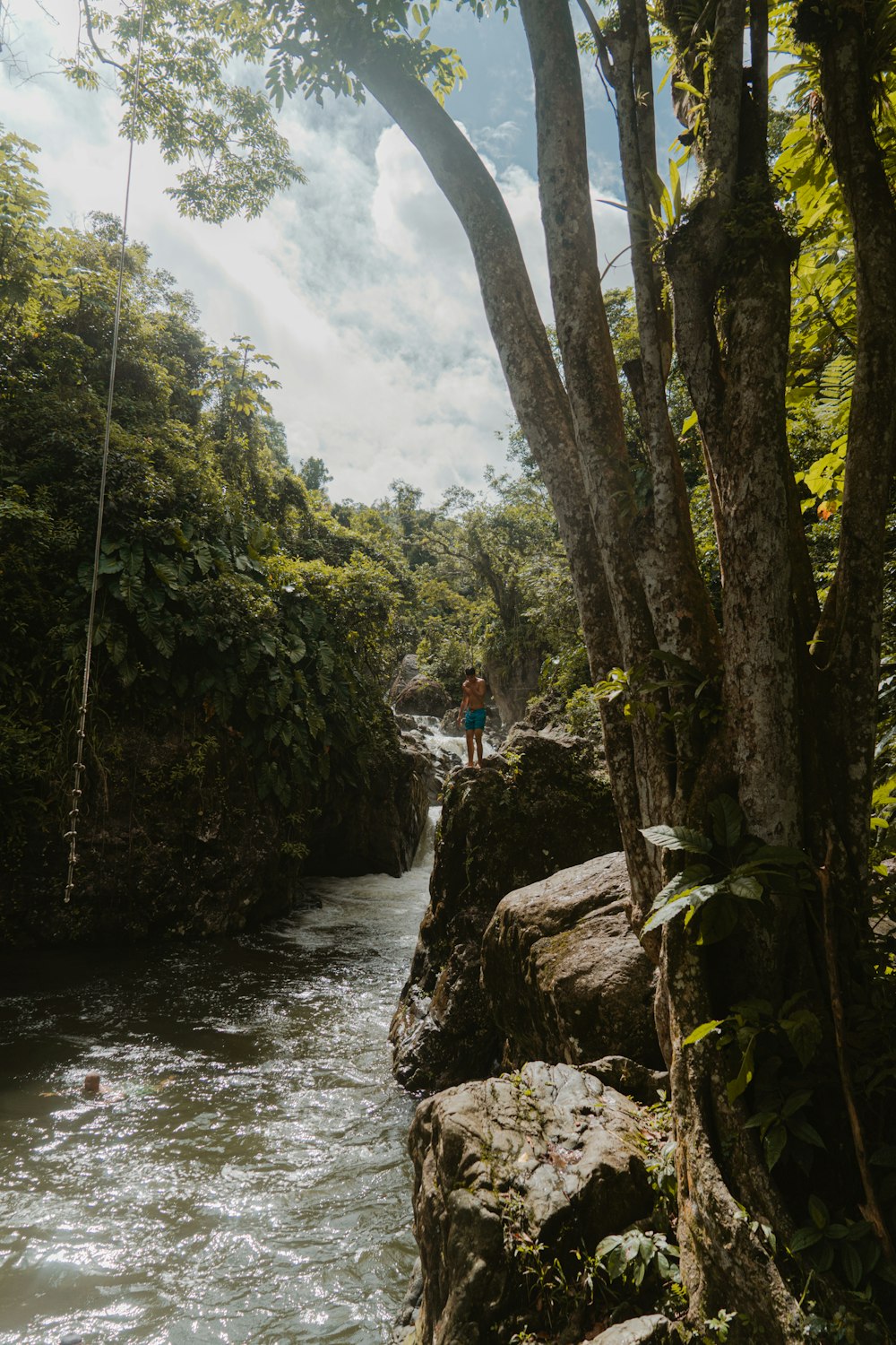 man in blue shirt and blue denim jeans standing on rock near river during daytime