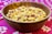 A wooden bowl filled with a mixed assortment of nuts and snacks, including peanuts and possibly chickpeas, placed on a vibrant pink patterned fabric.