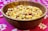 A wooden bowl filled with a mixed assortment of nuts and snacks, including peanuts and possibly chickpeas, placed on a vibrant pink patterned fabric.