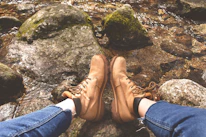 Close-up of durable hiking boots resting on a mossy rock beside a flowing stream.