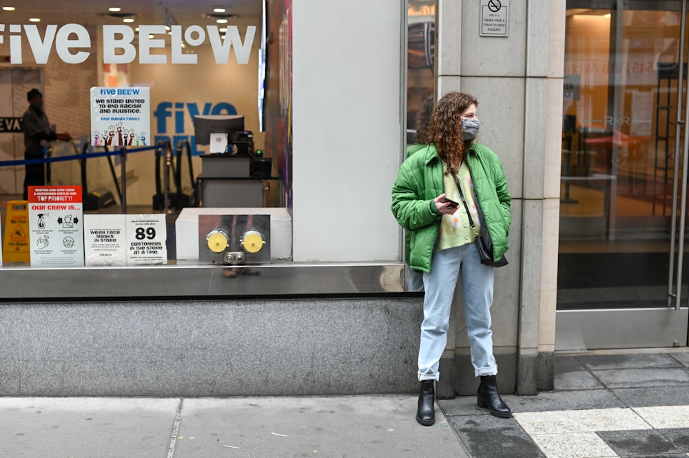 man in green jacket and white pants standing near brown and white store