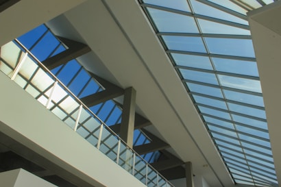 A modern architectural design featuring a series of large glass panels set in a geometric pattern. The structure includes strong lines and angular shapes, creating an expansive and airy space with natural light streaming through the transparent ceiling.