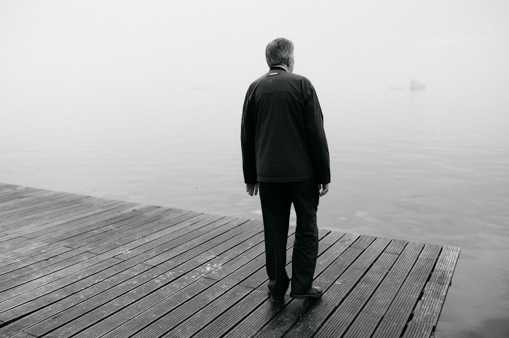 man in black coat standing on wooden dock