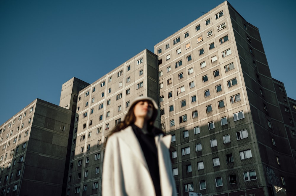 woman in white coat standing near white concrete building during daytime