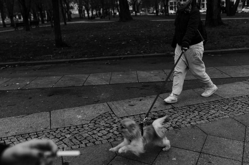 grayscale photo of man walking with dog on street