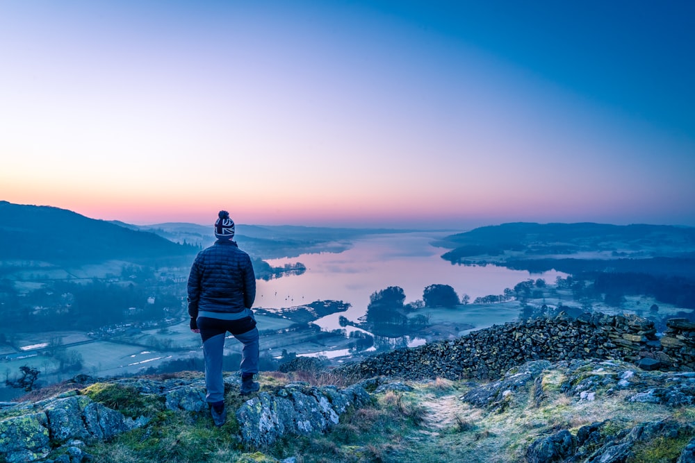 man in black jacket standing on rock formation looking at the sea during daytime