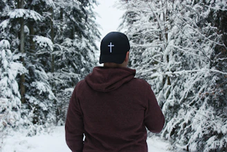 person in red hoodie and black cap standing on snow covered ground