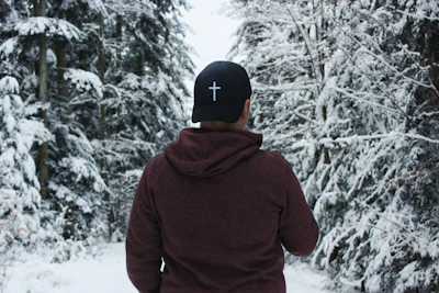 person in red hoodie and black cap standing on snow covered ground