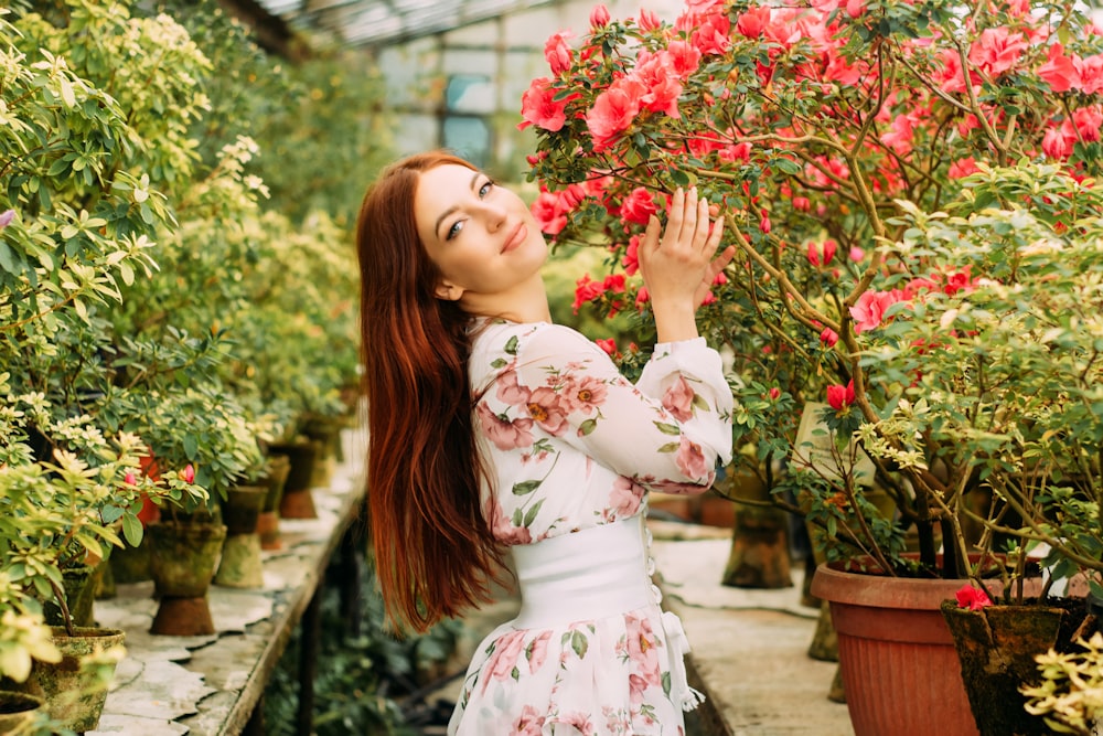 woman in white and red floral dress standing beside red flowers during daytime