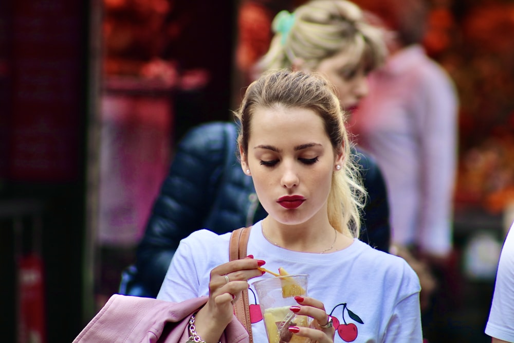 fille en t-shirt à col rond blanc tenant un gobelet en plastique blanc et rouge