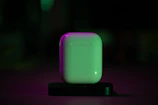Close-up of neon blue silicone AirPods case glowing softly on a dark surface.