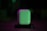 A white charging case, resembling one used for wireless earbuds, is illuminated with green and purple lighting, creating a dramatic and stylish effect. It is centered on a dark background, enhancing the visibility of the object.