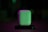 A white charging case, resembling one used for wireless earbuds, is illuminated with green and purple lighting, creating a dramatic and stylish effect. It is centered on a dark background, enhancing the visibility of the object.