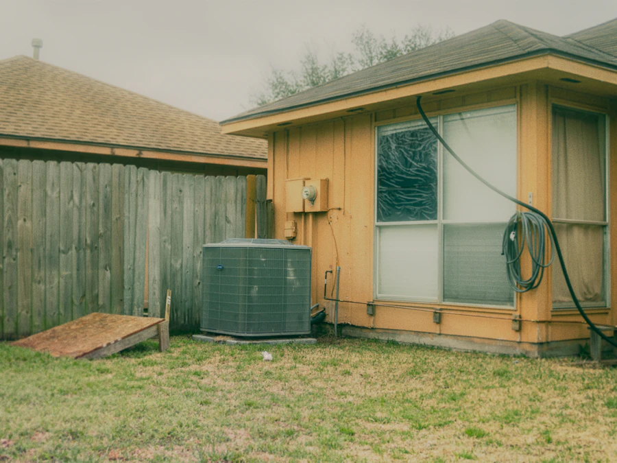 An AC condenser and power cord in a fenced backyard