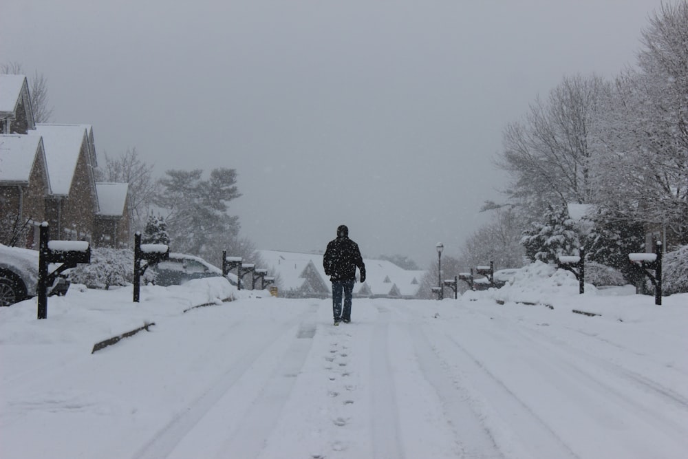 person in black jacket walking on snow covered road during daytime