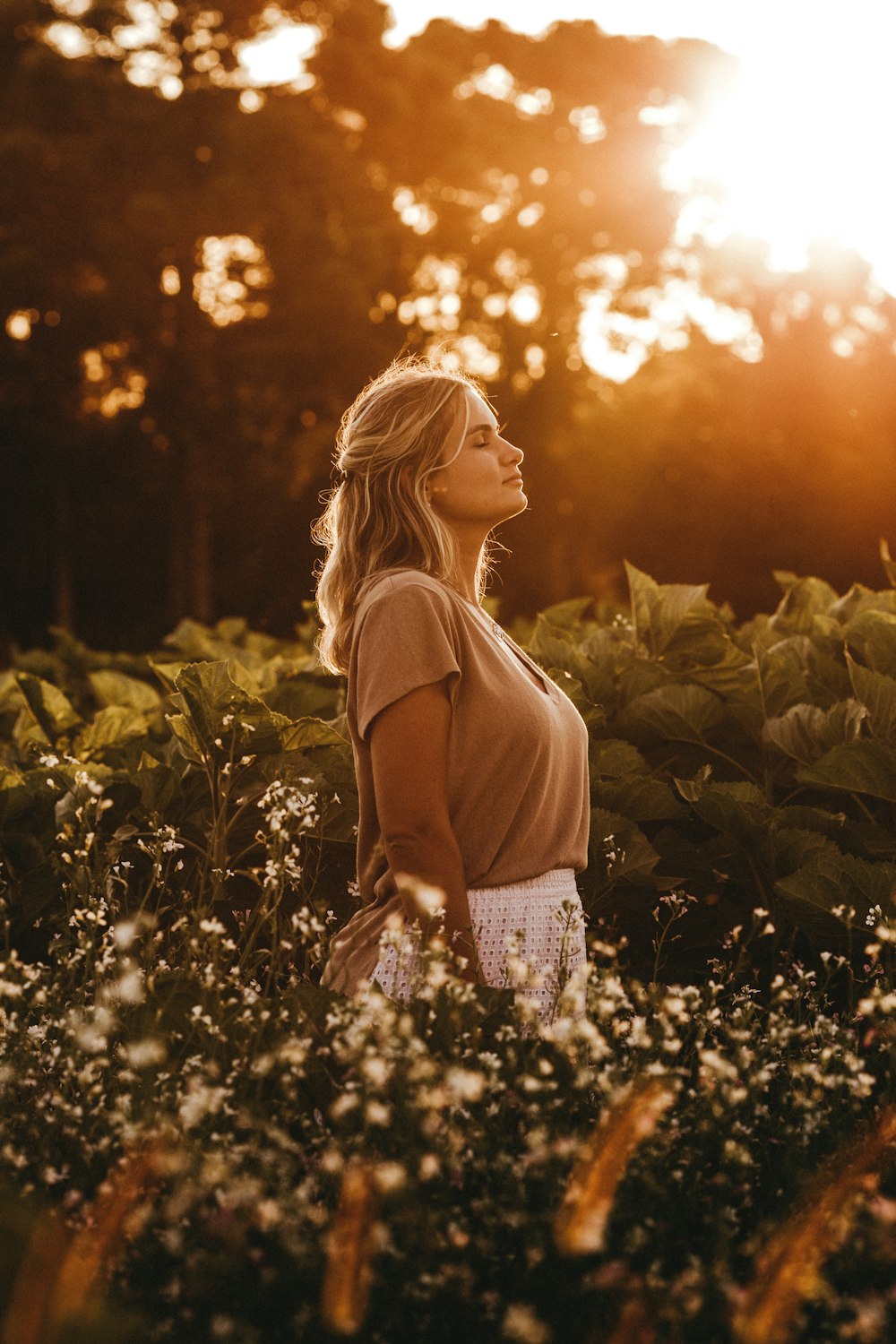 femme en débardeur marron debout sur le champ d’herbe verte au coucher du soleil