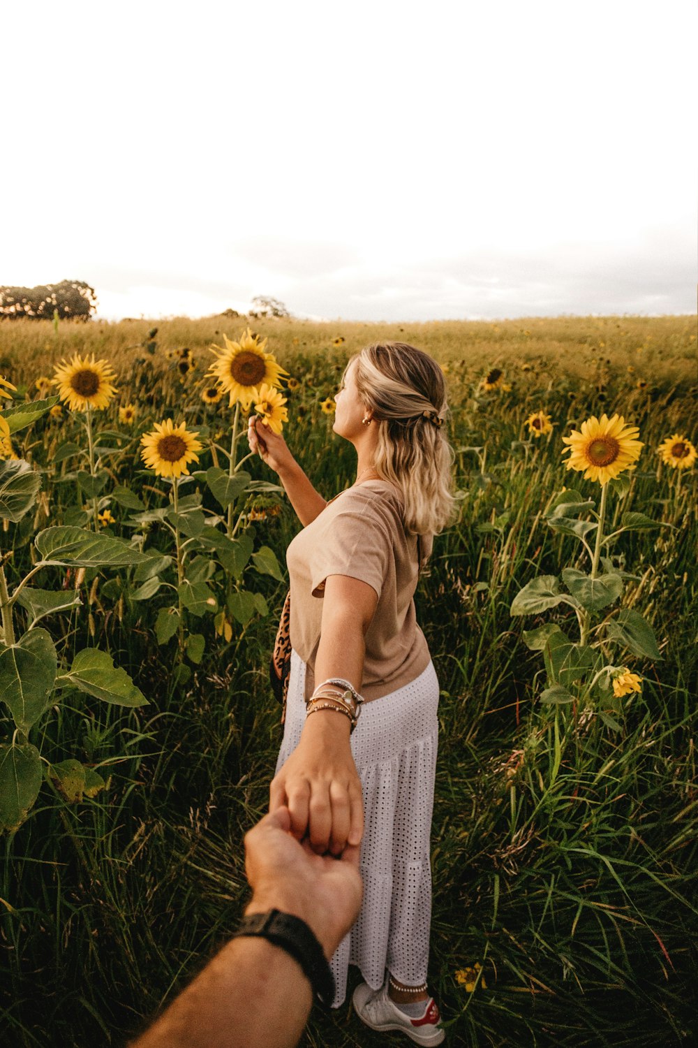 woman in white tank top standing on sunflower field during daytime