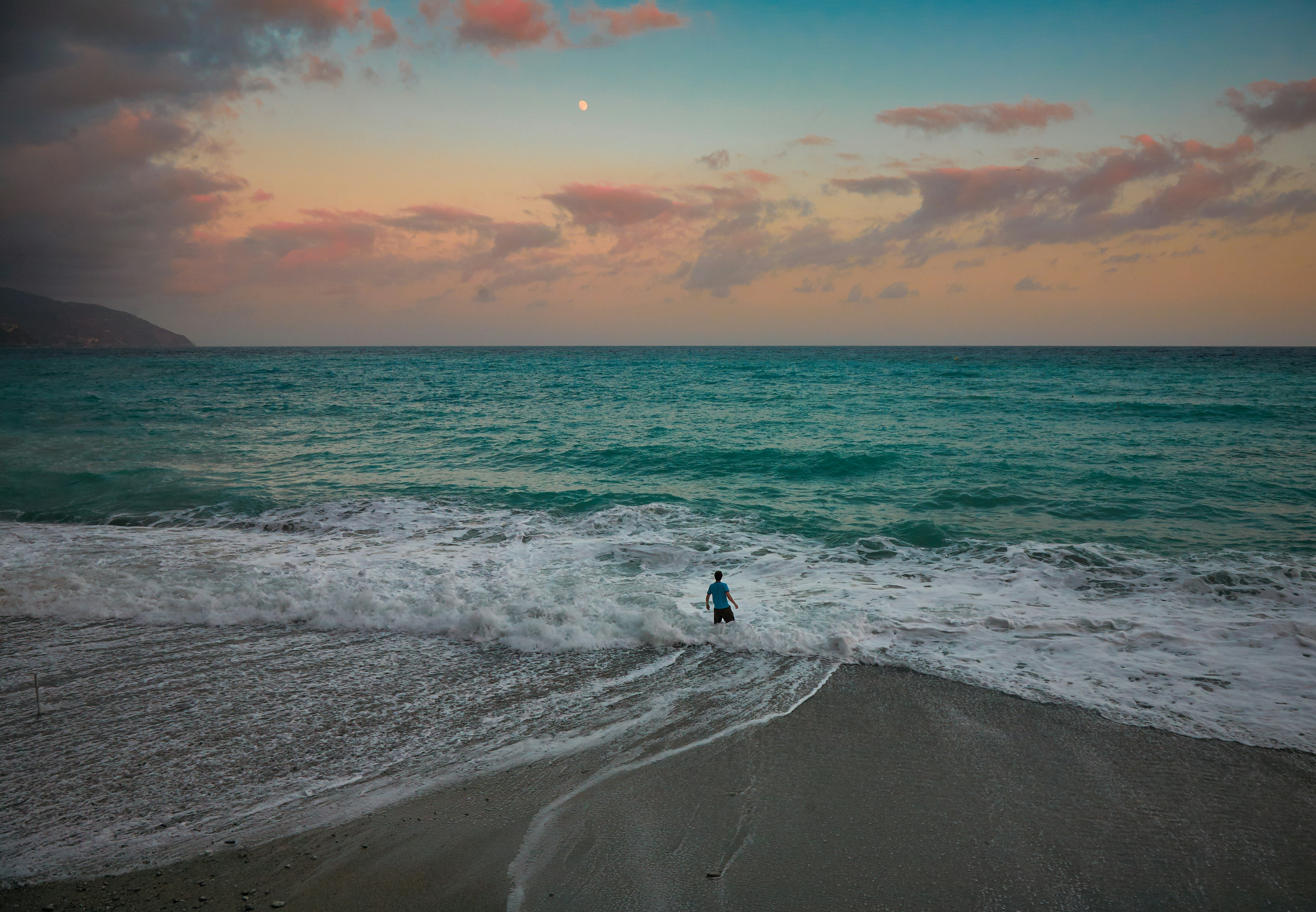 person in black shirt and pants standing on seashore during sunset