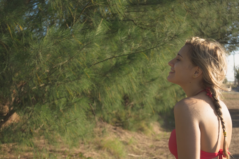 woman in red tank top standing near green trees during daytime