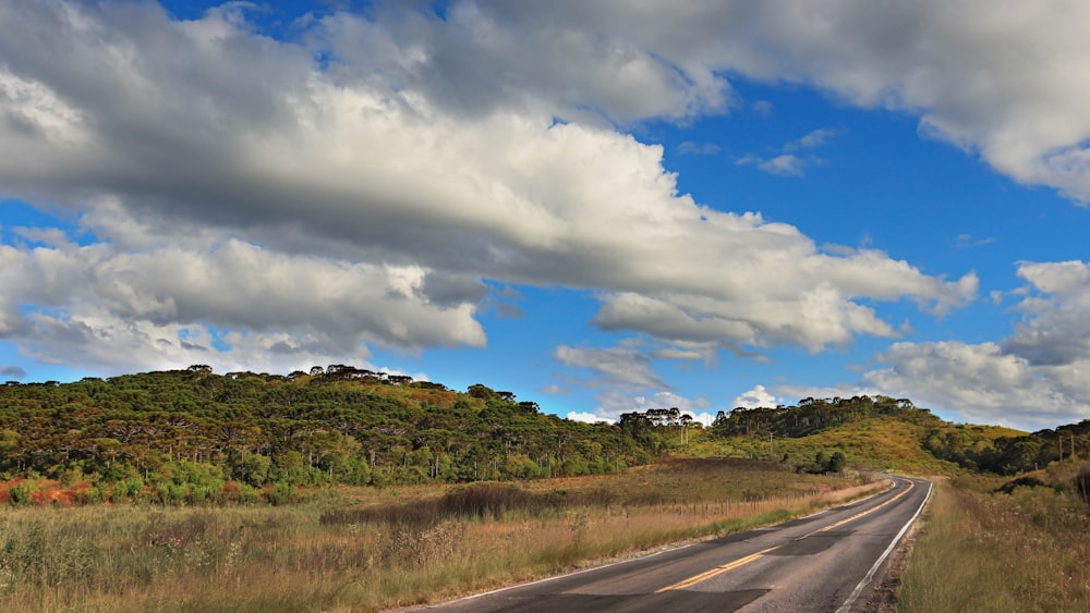 estrada de asfalto cinza entre campo de grama verde sob céu nublado azul e branco durante o dia