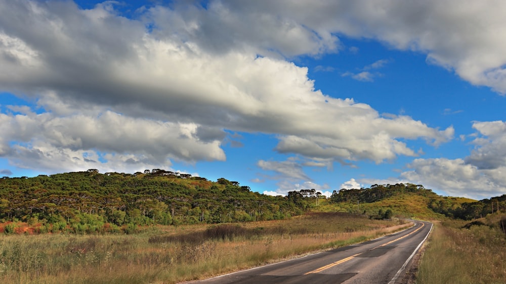 Carretera de asfalto gris entre campo de hierba verde bajo cielo nublado azul y blanco durante el día