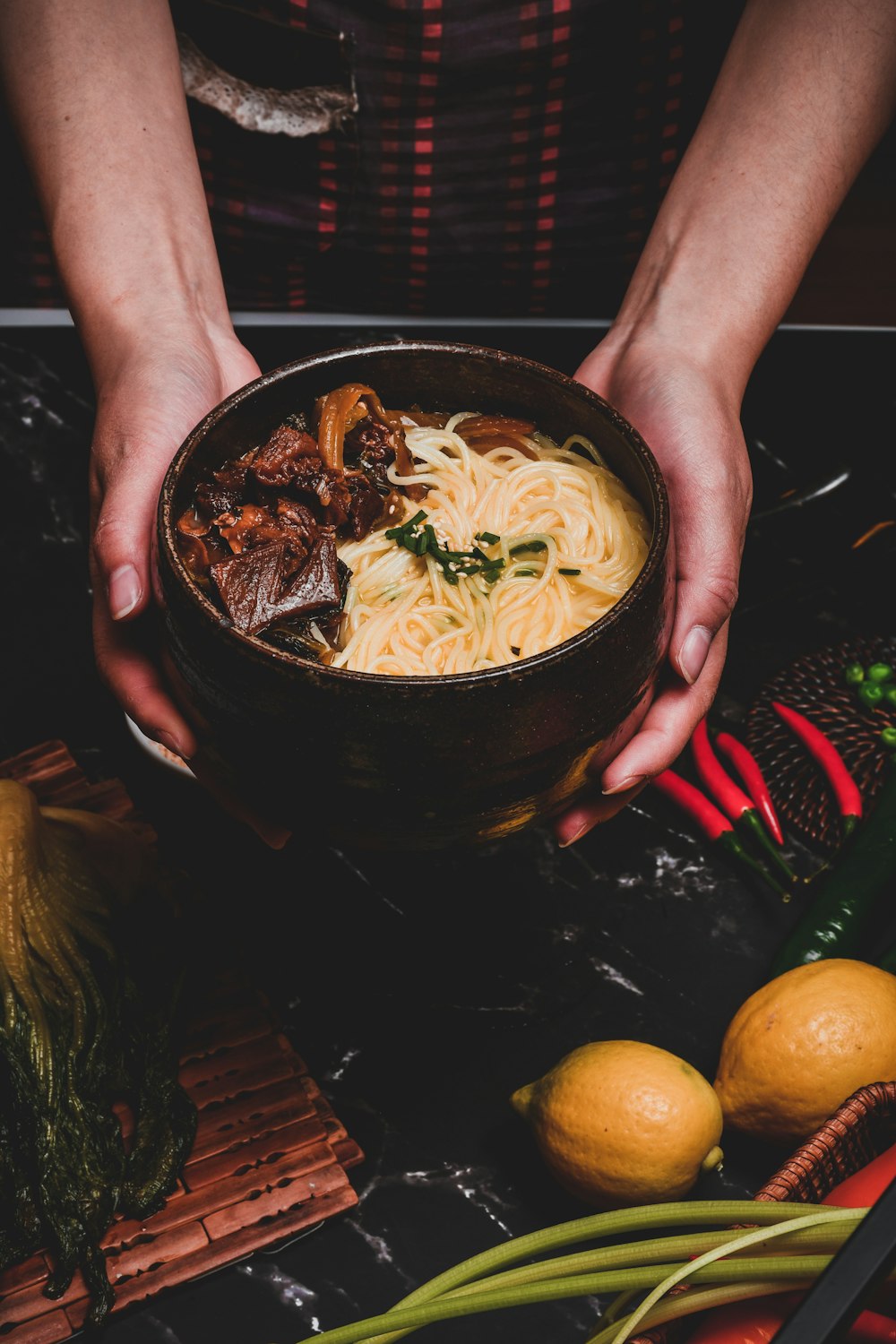 person holding black ceramic bowl with noodles and orange fruit