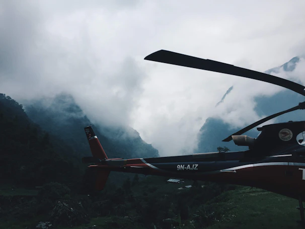 A helicopter soaring above misty valleys and rugged peaks at sunrise.