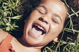 Close-up of a child’s joyful expression as they play in sun-dappled grass.