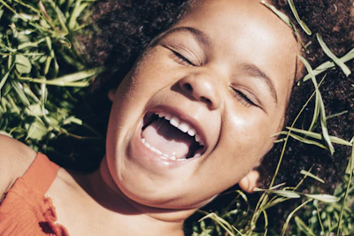 Close-up of a child’s joyful expression as they play in sun-dappled grass.