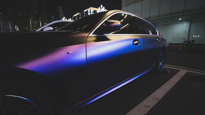A sleek modern car parked under city lights at night, reflecting the dark color theme.