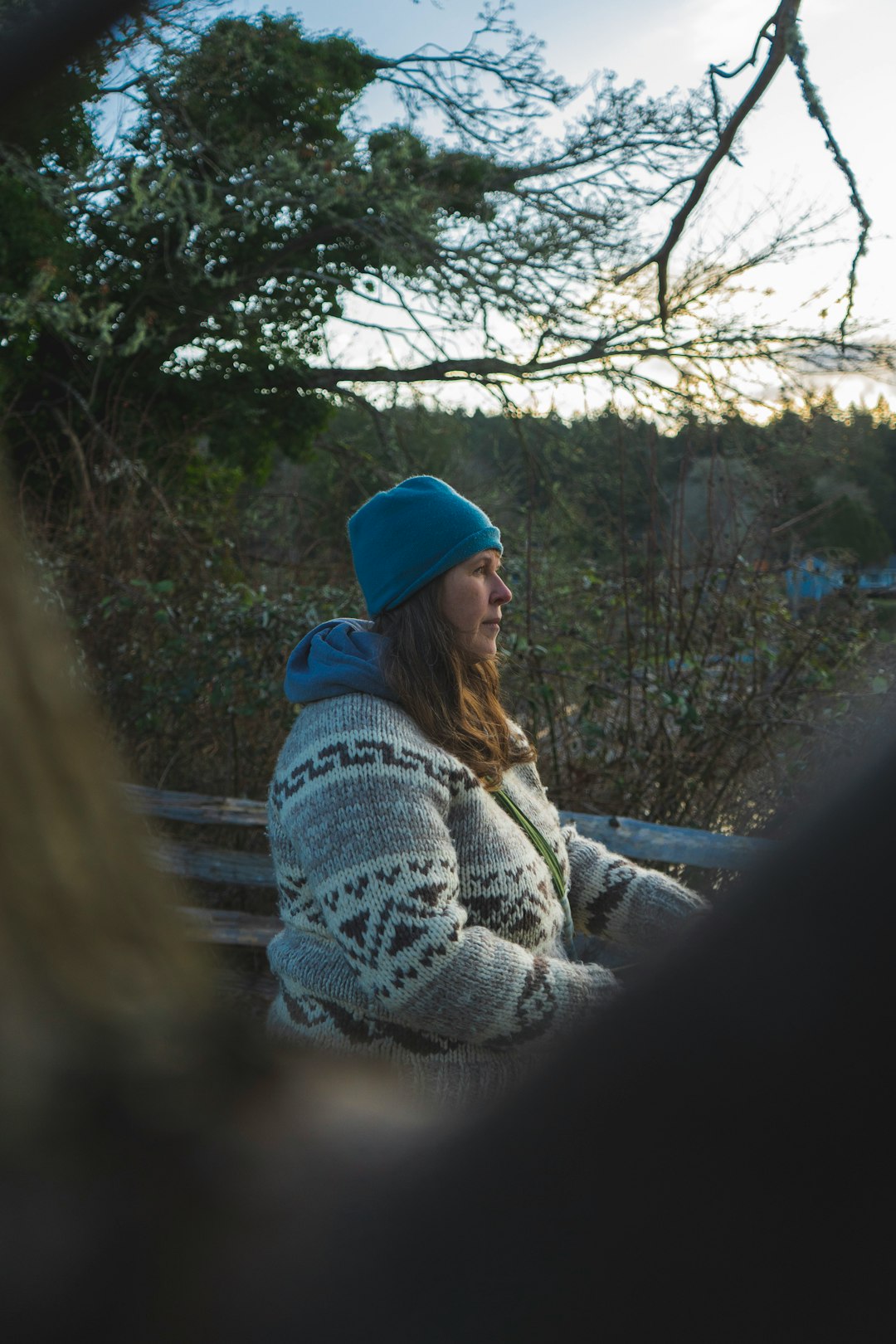 woman in white and black sweater and blue knit cap sitting on brown wooden bench during