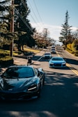 A panoramic shot of a convoy of luxury cars lined up on a scenic road at sunset.