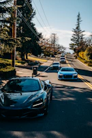 A panoramic view of a convoy of supercars driving through a mountain pass at dawn.
