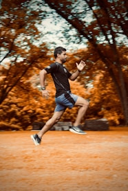 man in black t-shirt and black shorts running on brown field