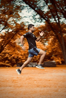man in black t-shirt and black shorts running on brown field