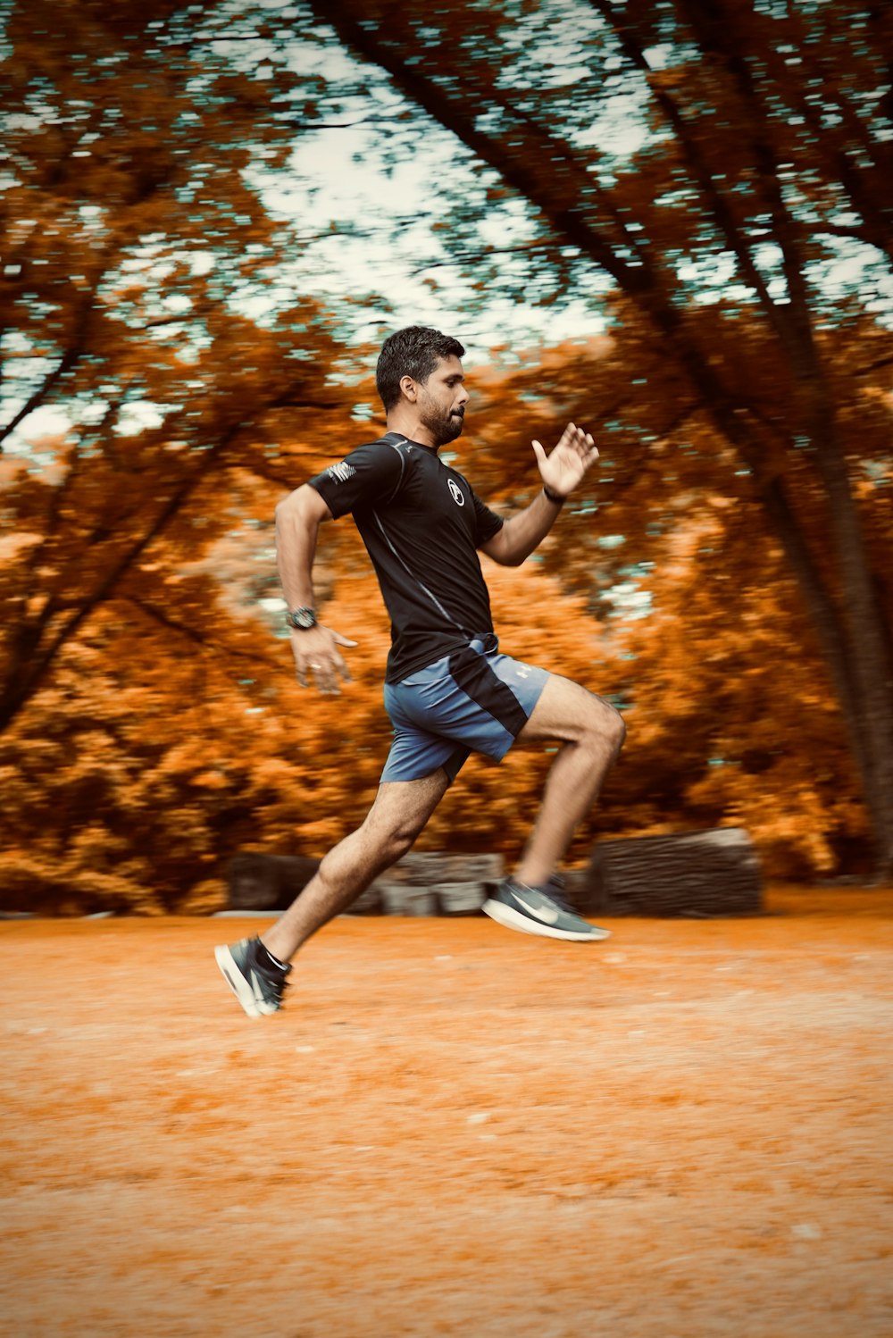 Hombre con camiseta negra y pantalones cortos negros corriendo en campo marrón