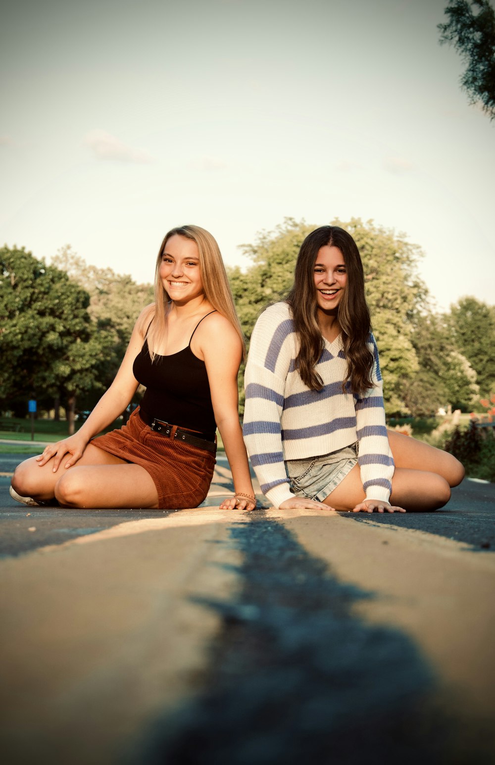 2 women sitting on concrete pavement during daytime