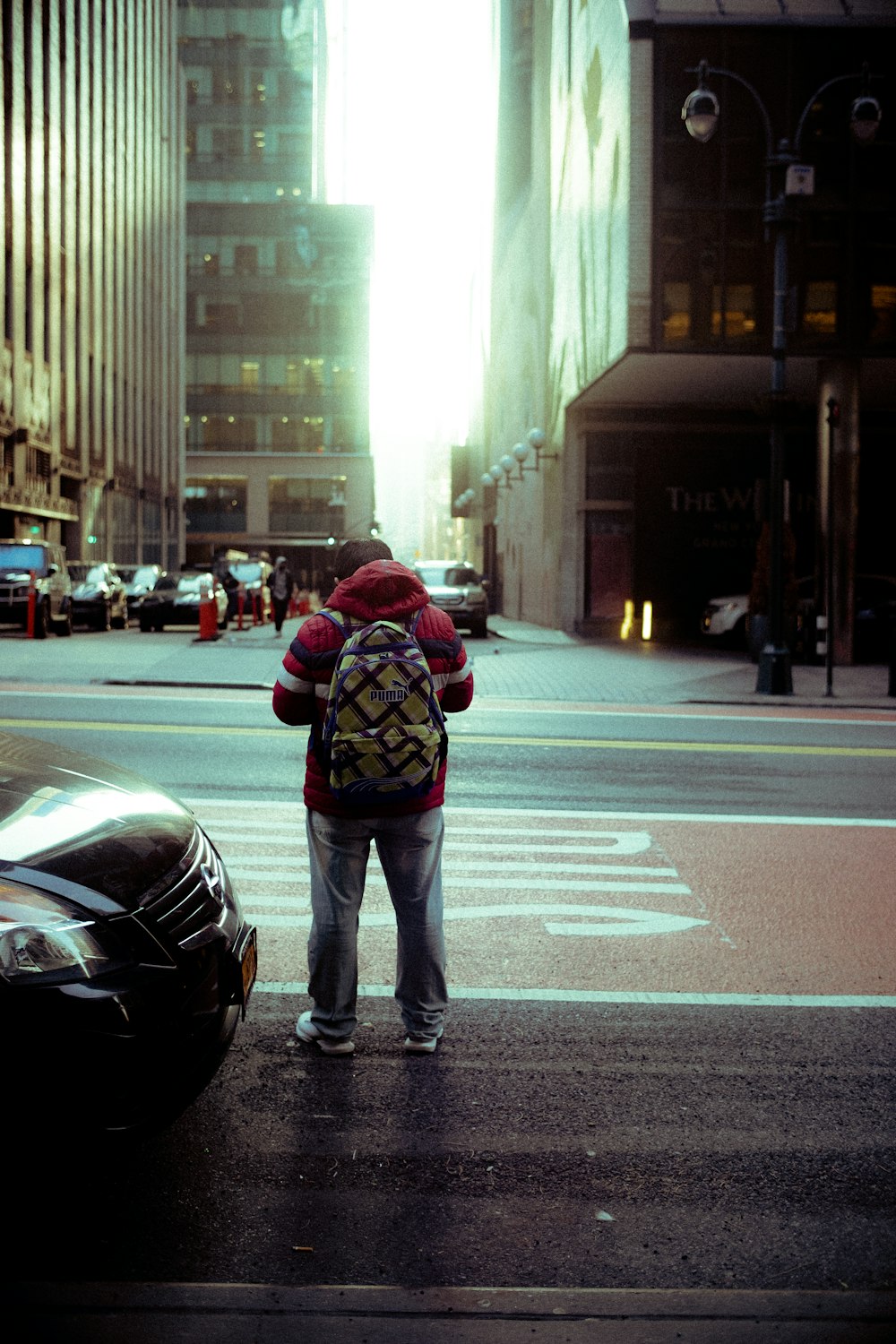 man in black jacket and blue denim jeans standing on pedestrian lane during daytime