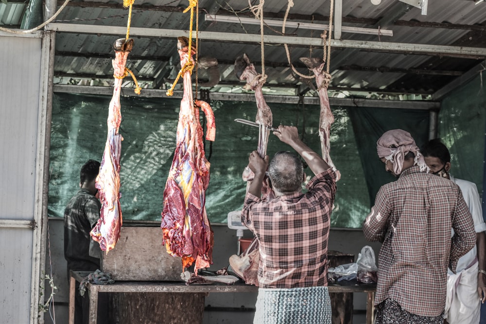 homme en chemise à carreaux blanc et rouge debout à côté de la viande