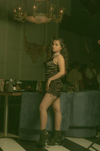 A sensual woman in elegant evening wear, smiling softly in a dimly lit room.