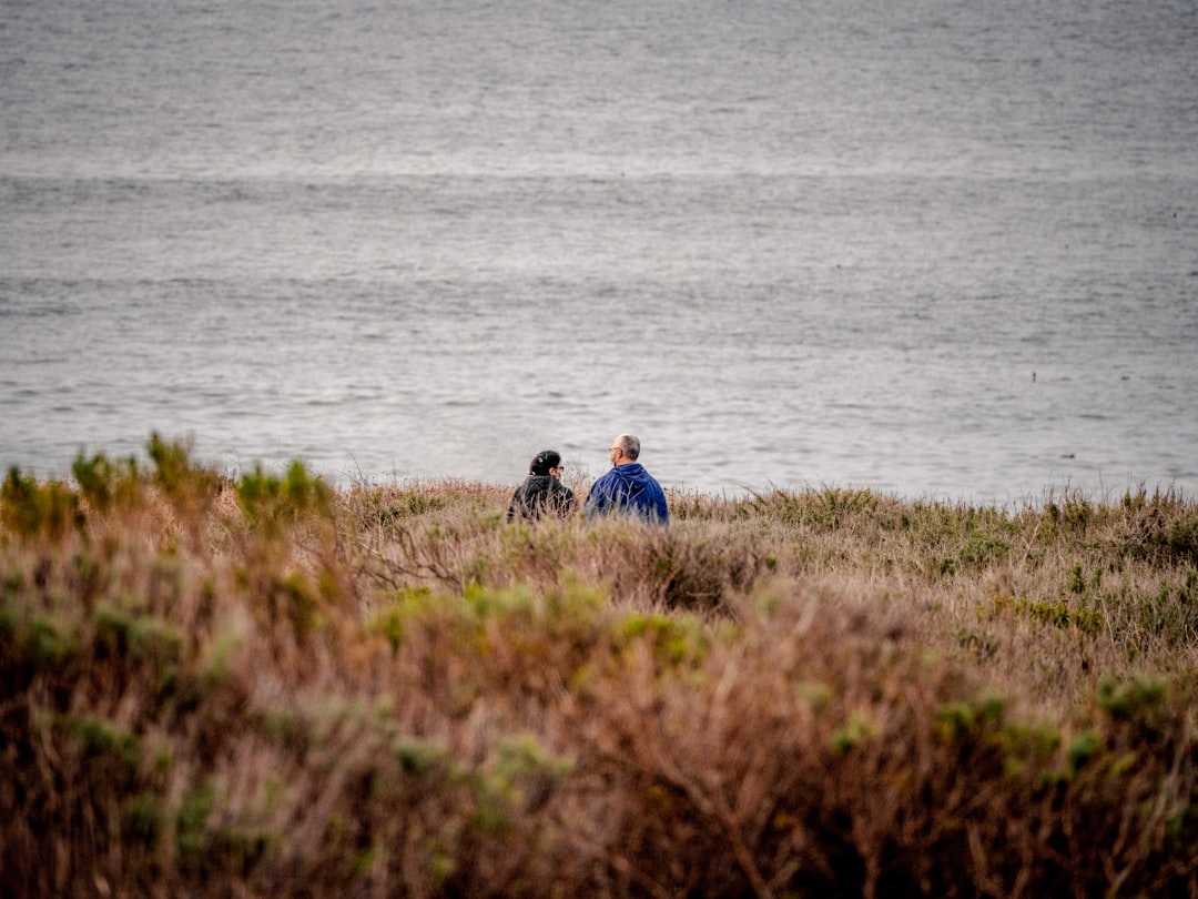 man and woman sitting on grass field near body of water during daytime