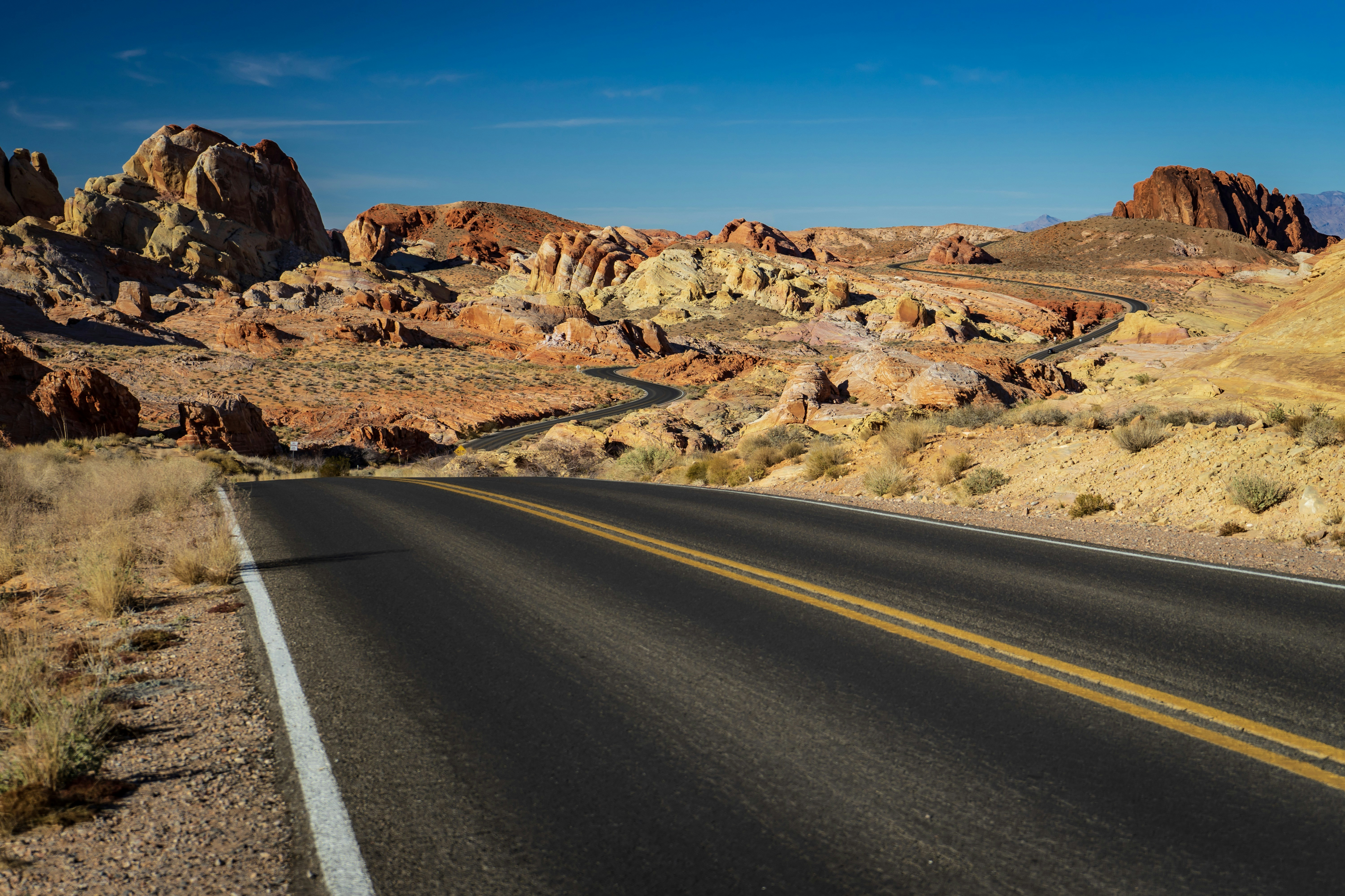 gray asphalt road between brown rock formation under blue sky during daytime, 
