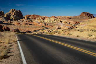 gray asphalt road between brown rock formation under blue sky during daytime