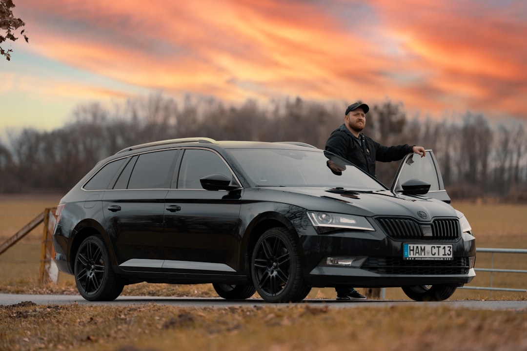 man in black jacket standing beside black bmw m 3